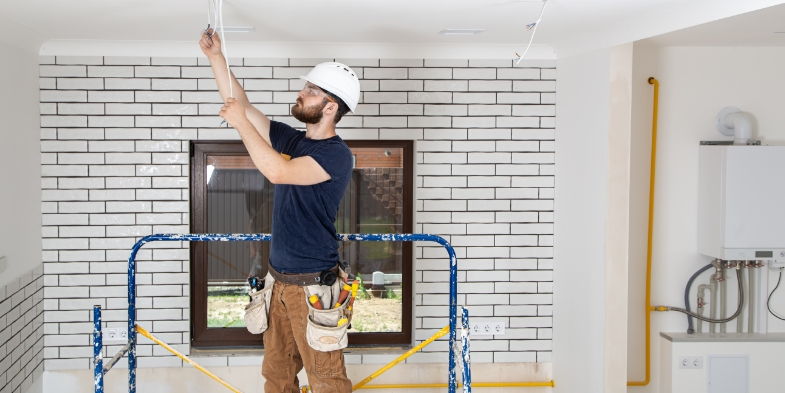 man in hardhat working on electrical in a home ceiling