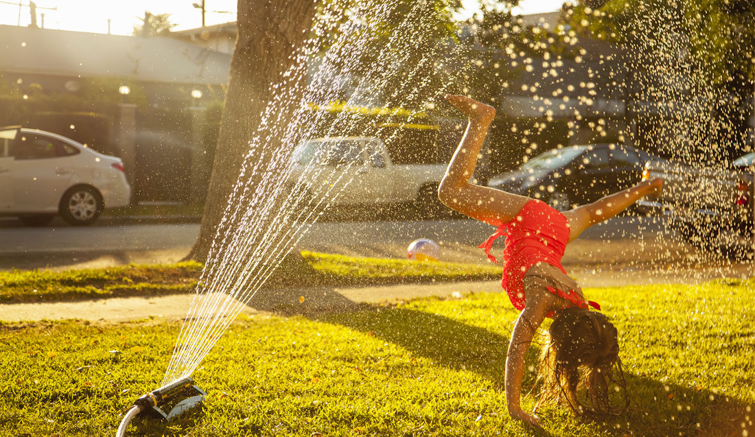 girl playing in sprinkler on hot day